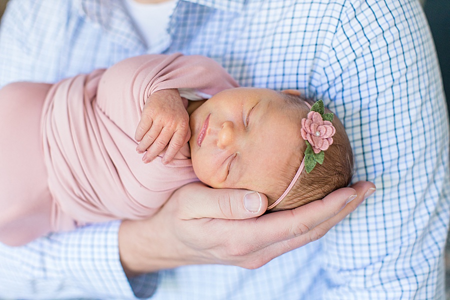 dad holding newborn girl head in pink wrap with flower in hair