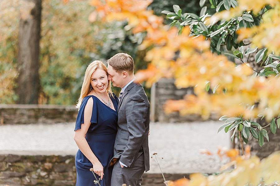 couple snuggling with fall leaves in december navy dress and grey suit