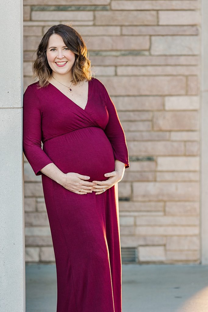 mom holding baby bump in maroon dress