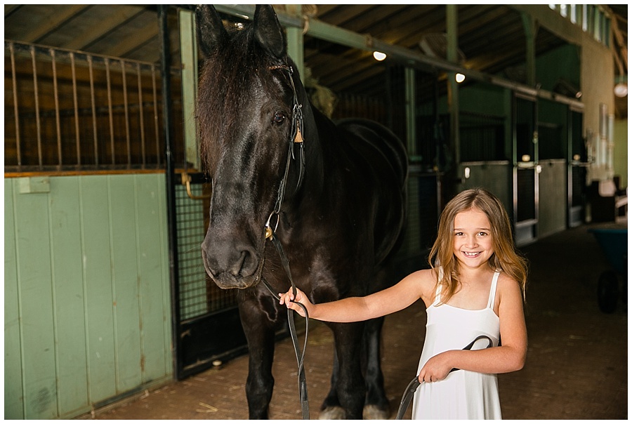 girl in white dress with black horse in barn