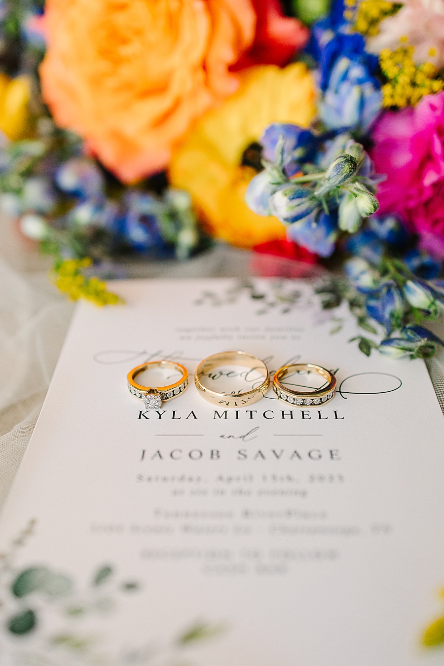 Gold wedding rings on invitation with colorful wedding bouquet