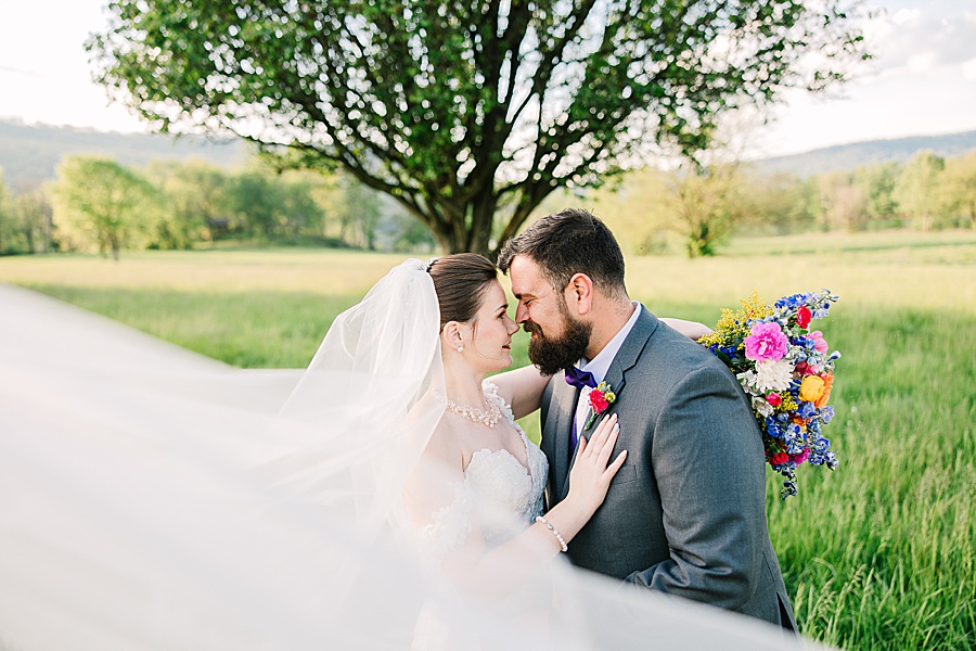 Bride and groom embracing in bridal veil with vibrant floral bouquet