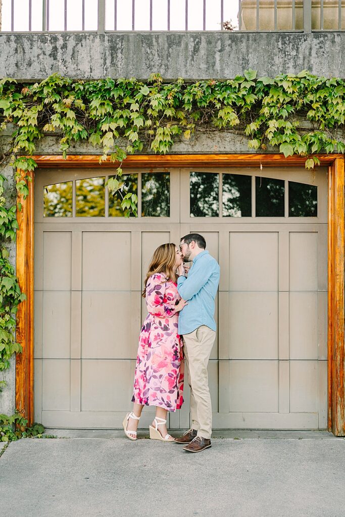 coule kissing in front of a garage door with ivy hanging on the walls during their engagement session