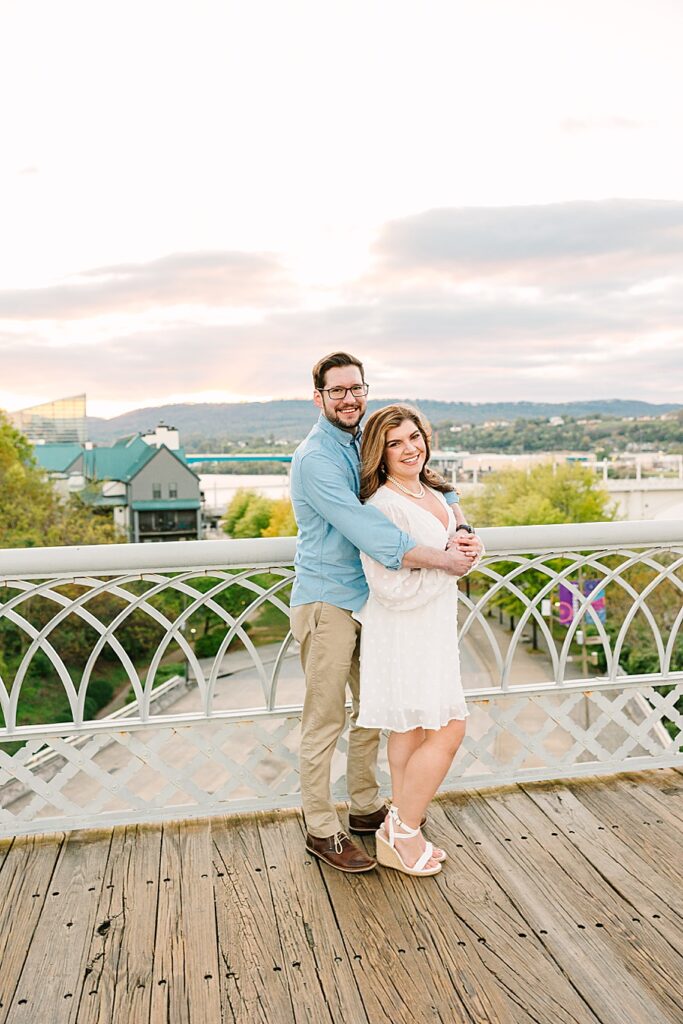 couple embracing during sunset on the walnut street pedestrian bridge overlooking the Tennessee river in downtown chattanooga during their engagement session 