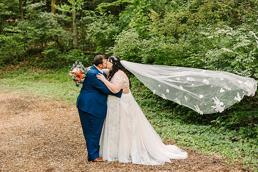 bride and groom kissing with veil flowing behind