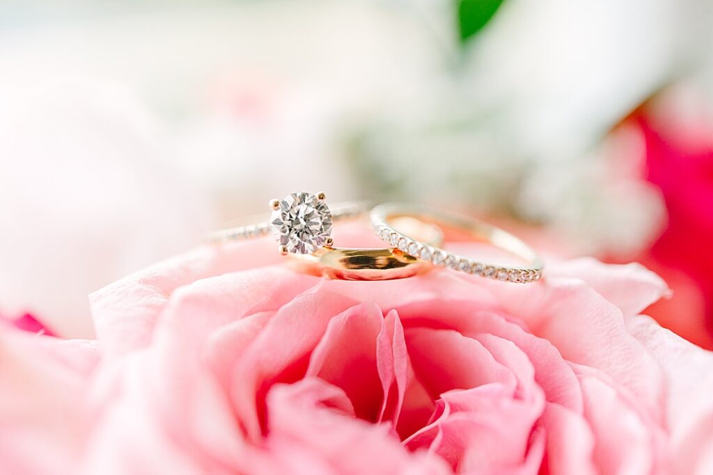 detail macro image of diamond wedding rings stacked on top of pink rose