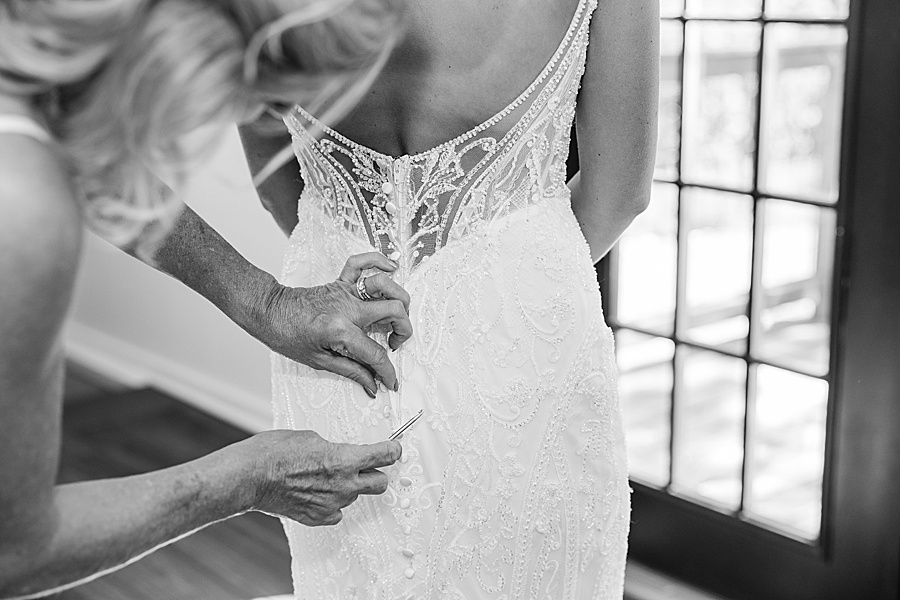 black and white image of mom buttoning up brides wedding dress