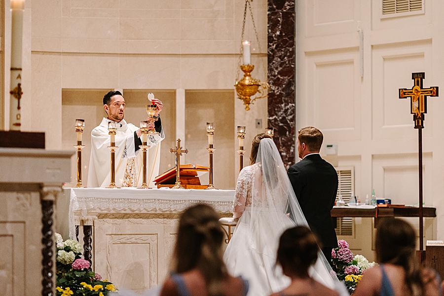 bride and groom with catholic priest before mass during ceremony