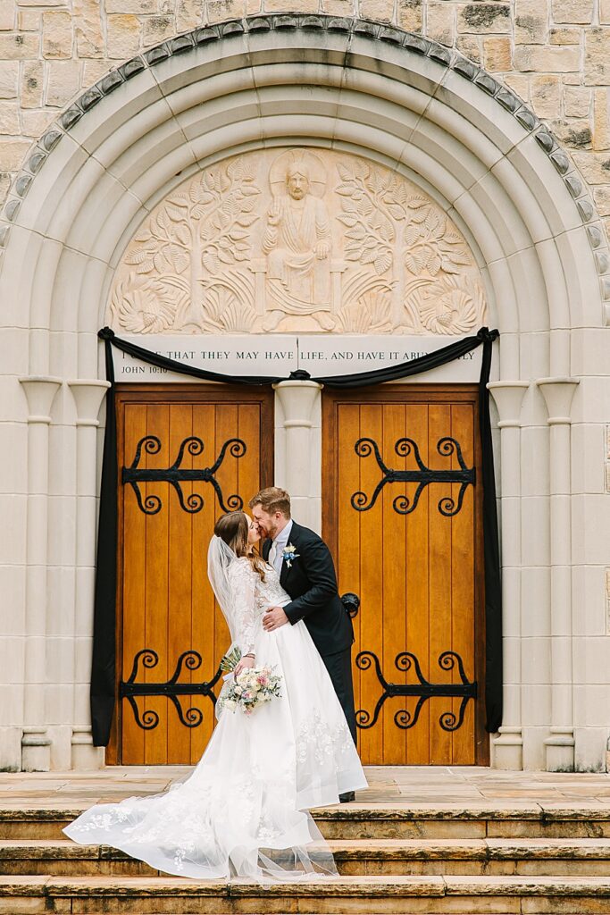 bride and groom kissing on steps of catholic church