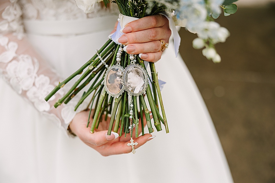bride holding bouquet with images of loved ones and a rosary around the bottom of bouquet