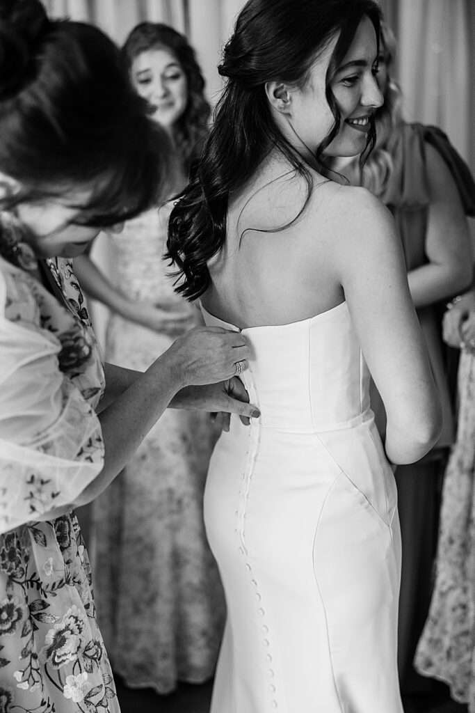 black and white image of mom buttoning up bride's wedding dress