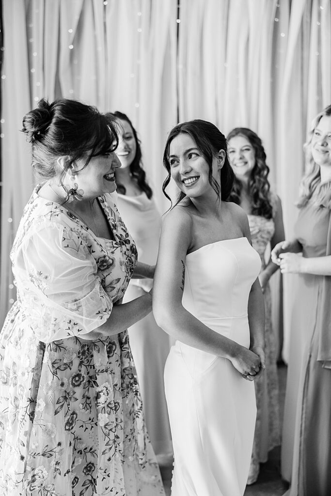 black and white image of bride looking back at mom while helping her to get dressed on her wedding day