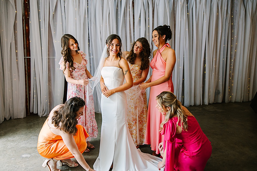 bridesmaids fluffing and helping bride getting dressed on wedding day at venue at the bluffs