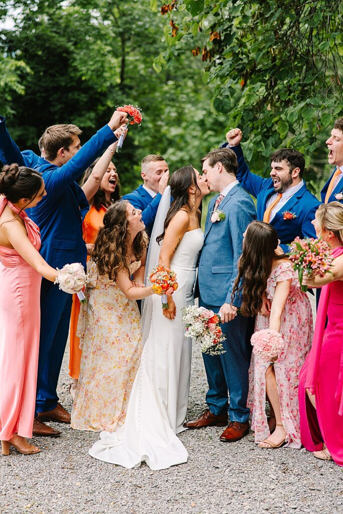 bride and groom kissing with bridal party cheering them on at venue at the bluffs