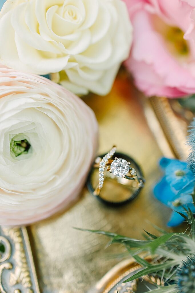 detailed wedding ring shot on gold tray with Ranunculus, garden roses, and delphinium