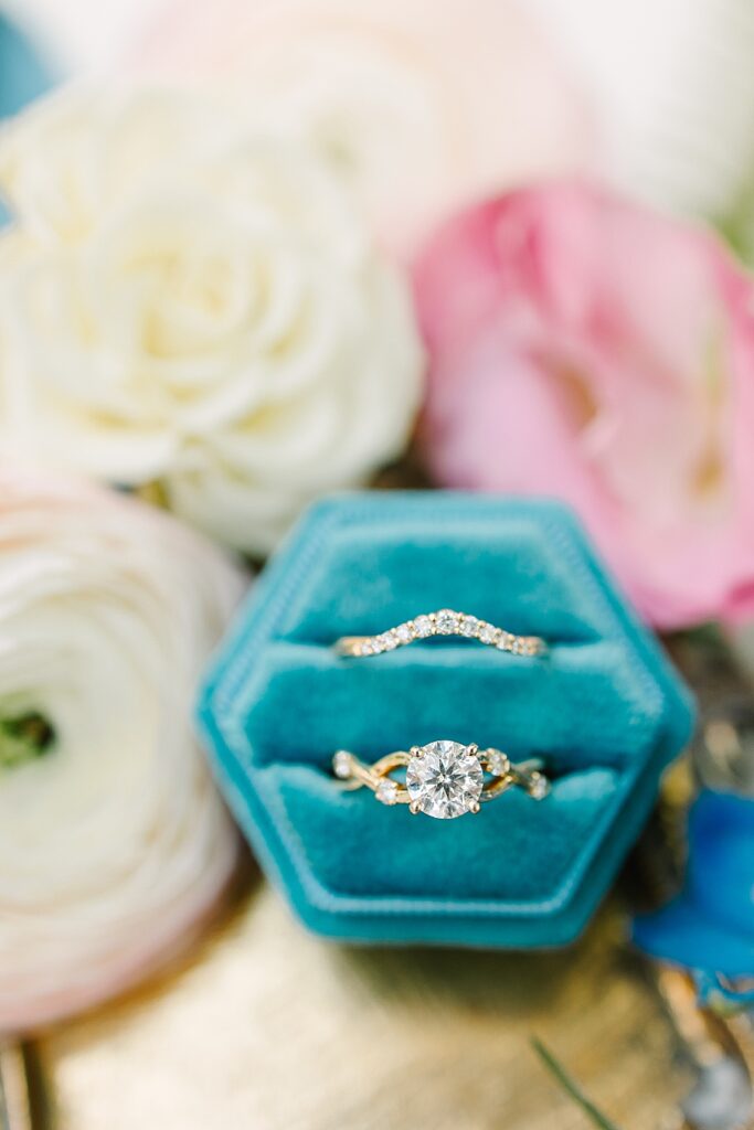 detailed wedding ring shot in blue velvet ring box with Ranunculus, garden roses, and delphinium