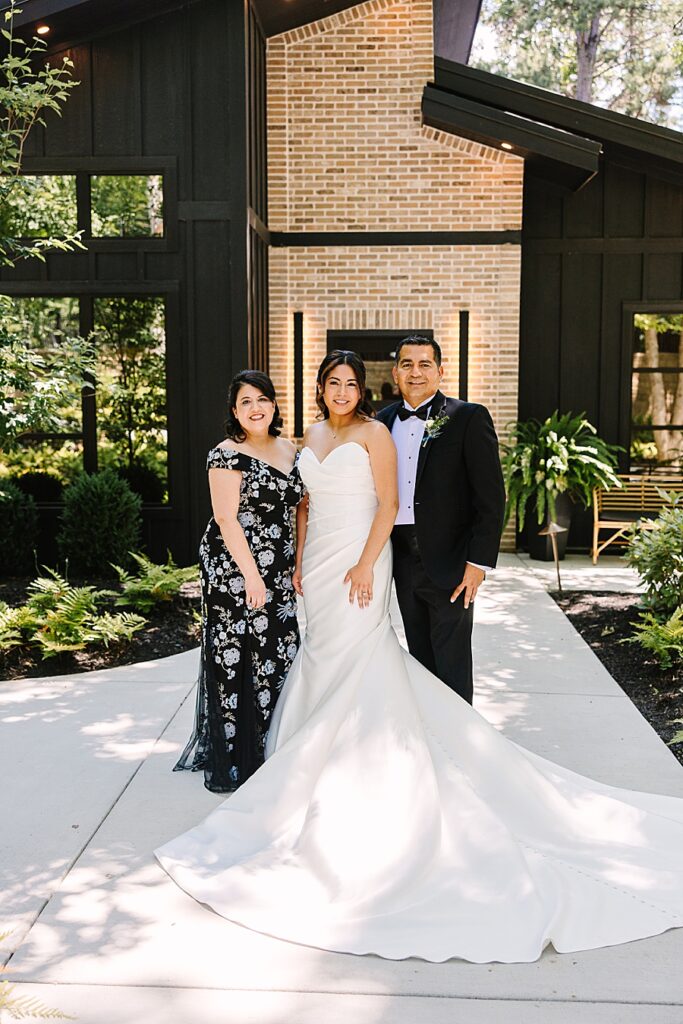 Bride with mom and dad on wedding day outside of bridal house at Glass house at Nichols Heir